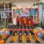 Group of children in colorful traditional indian outfits posing on a decorated janmashtami stage with marigold garlands umbrellas and a banner backdrop